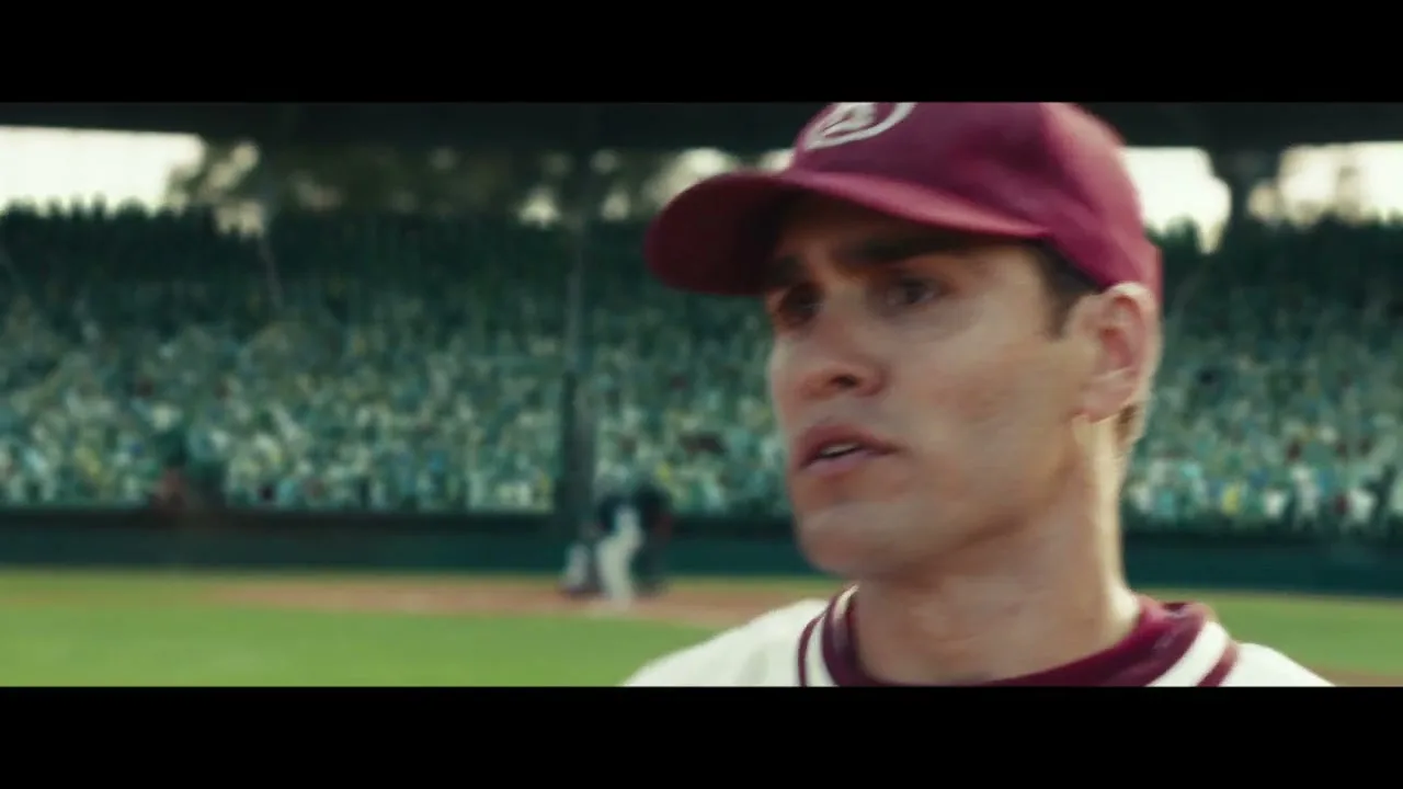 A male baseball player in a white and maroon uniform with a glove on his left hand, shouts and then turns his head to the right on a baseball field.