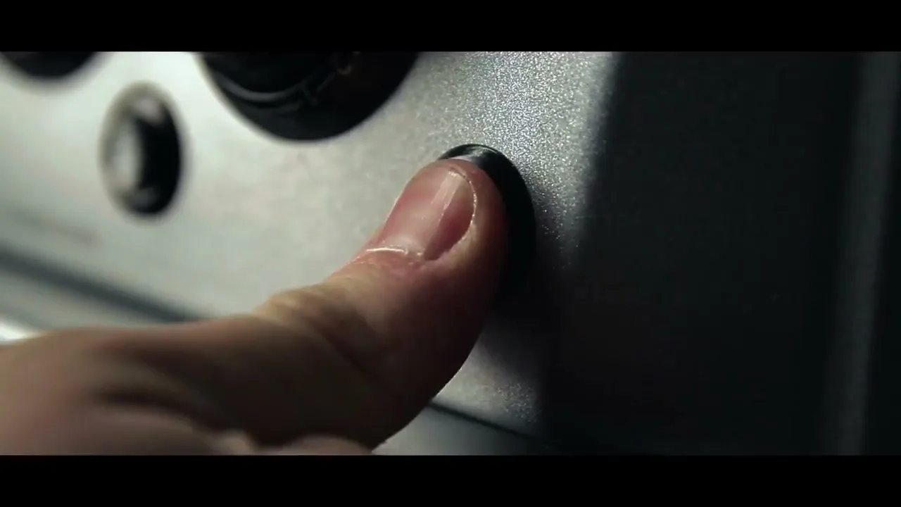 A close-up shot shows a person's finger pressing and turning a black knob with a white star on a silver kitchen appliance.