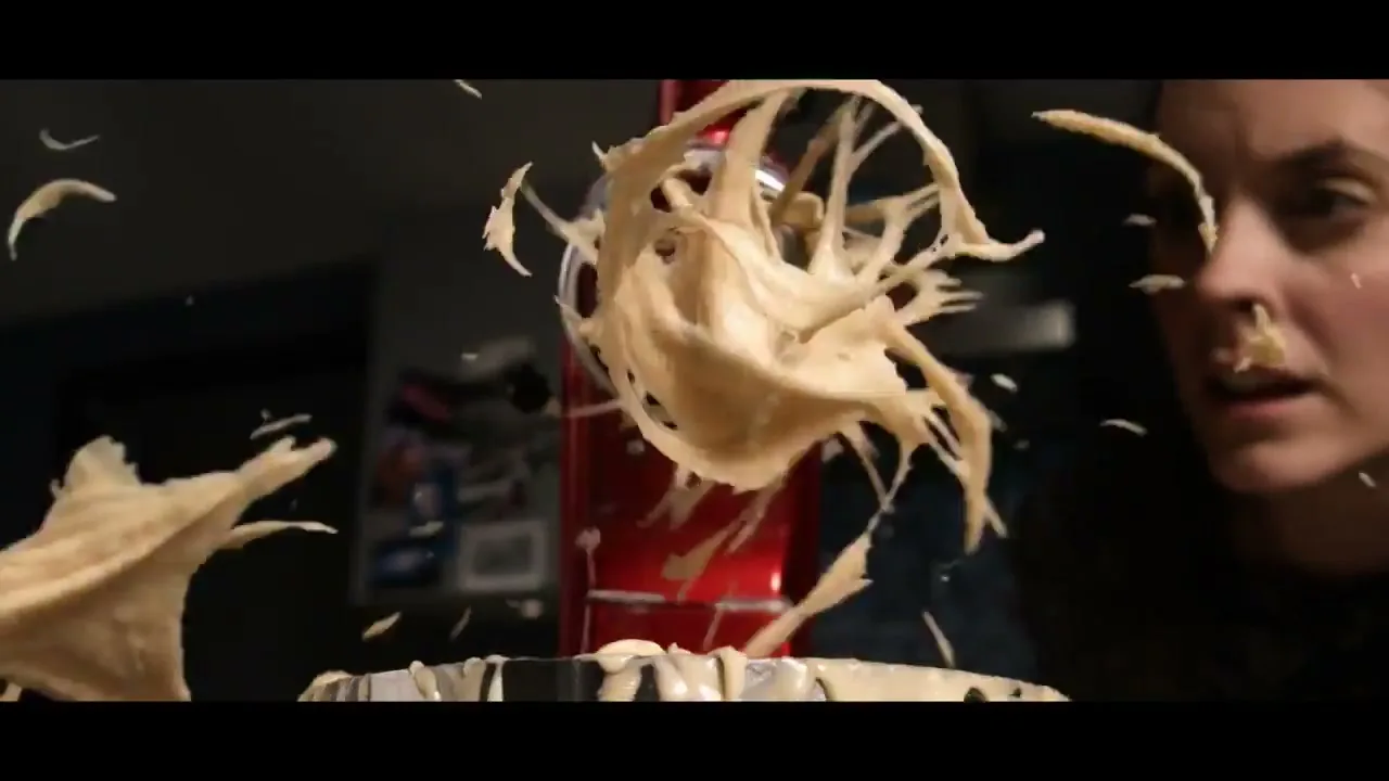 A woman looks on in surprise as batter explodes from a red stand mixer in a kitchen.