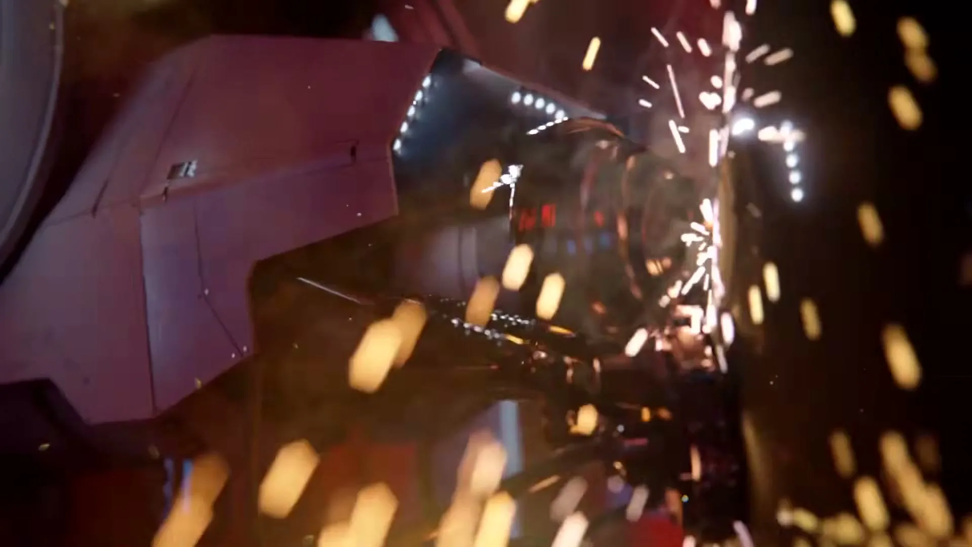 Sparks fly as a robotic arm grinds metal, creating a shower of bright orange and yellow light in a dark industrial setting.
