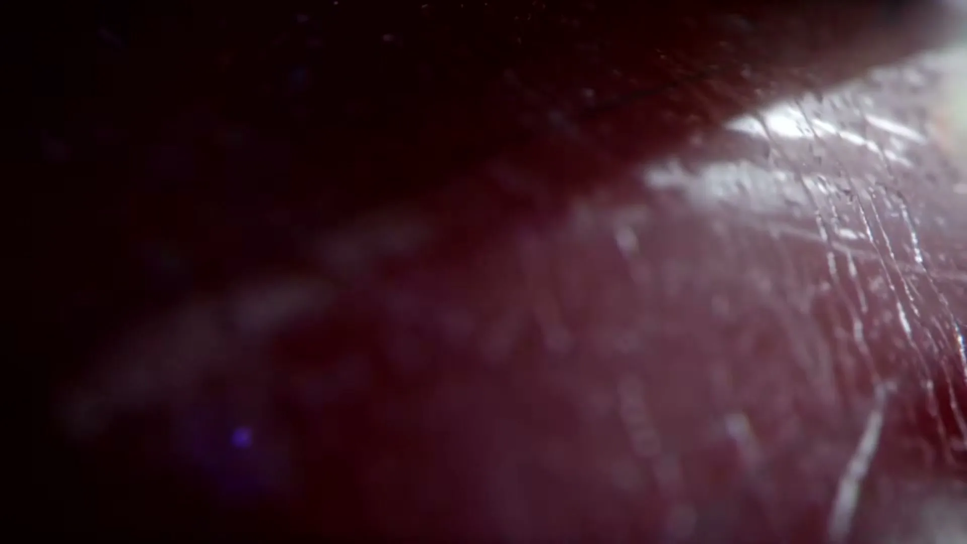 A macro shot shows a dark red surface with fine scratches and bright reflections, suggesting a metallic or polished material.