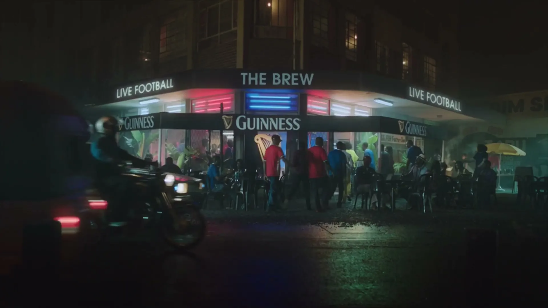 A bustling street scene at night shows people gathered outside a bar called "The Brew" with "Live Football" signs, as vehicles pass by.