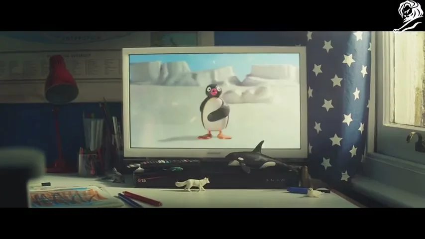 A claymation penguin dances on a TV screen, surrounded by a child's desk with toys and a star-patterned curtain, in a cozy room.