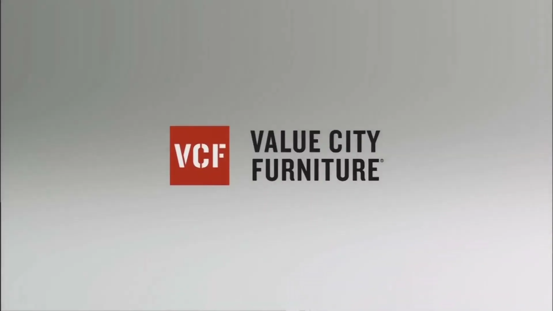The Value City Furniture logo, a red square with "VCF" in white, and "VALUE CITY FURNITURE" in black text, is displayed on a gray background.