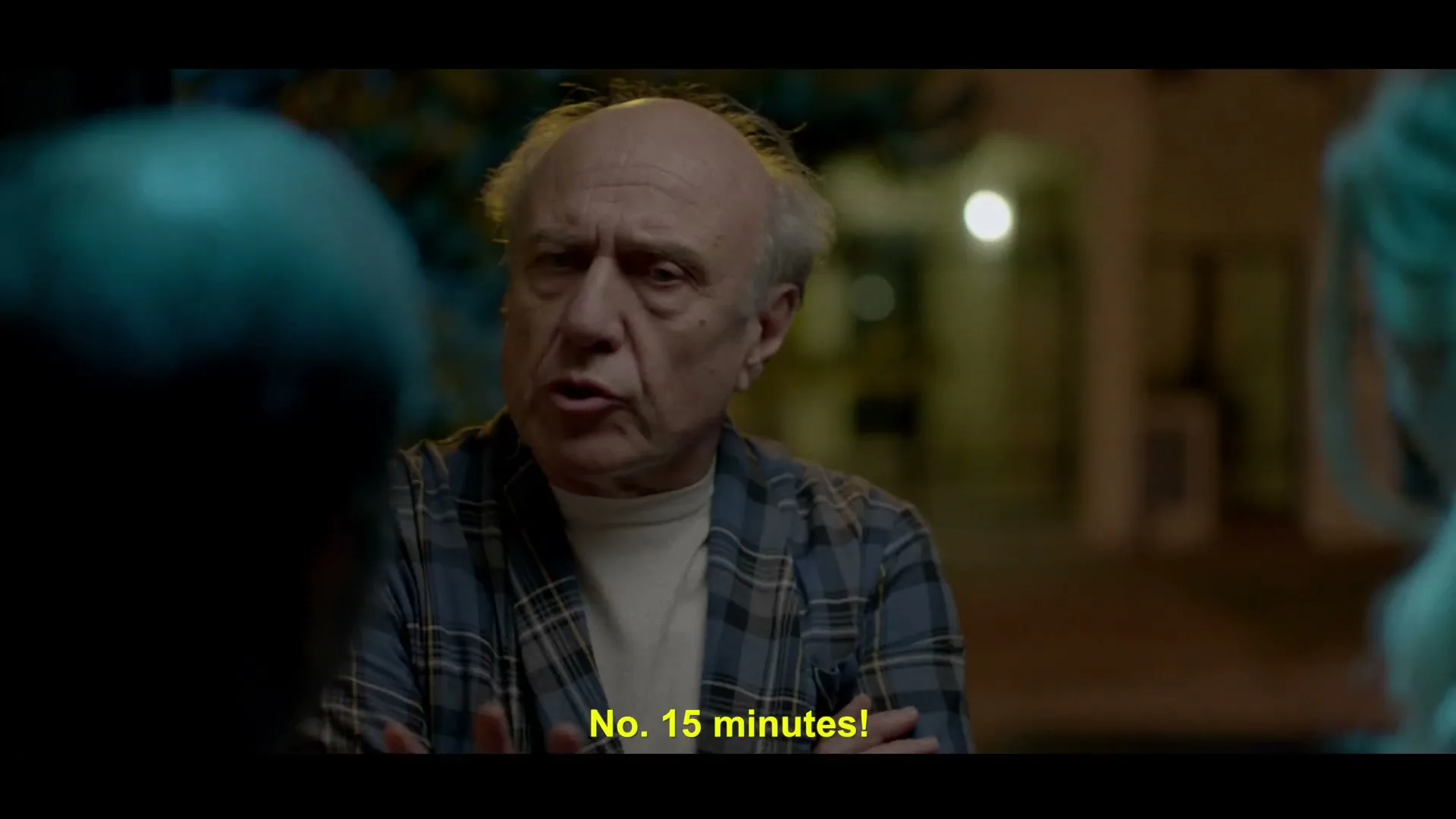 An older man in a plaid robe argues with two unseen people at night, gesturing with his hands.