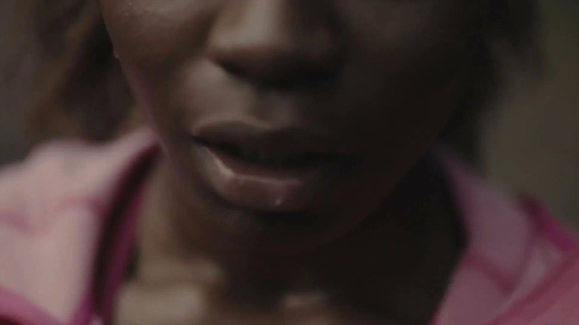 A young Black woman, wearing a pink athletic jacket, breathes heavily with sweat on her face, in a close-up shot.