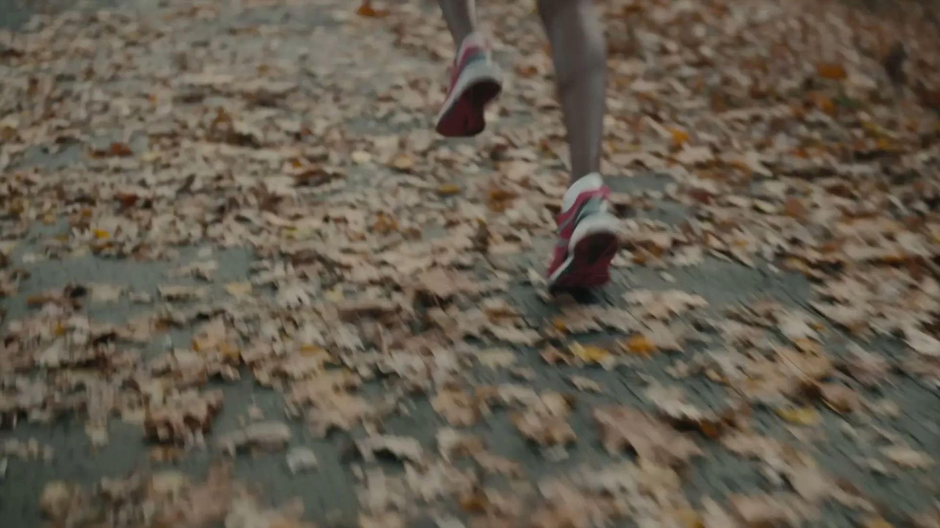 A young Black woman in a pink tracksuit runs through a sun-dappled forest path covered in autumn leaves.