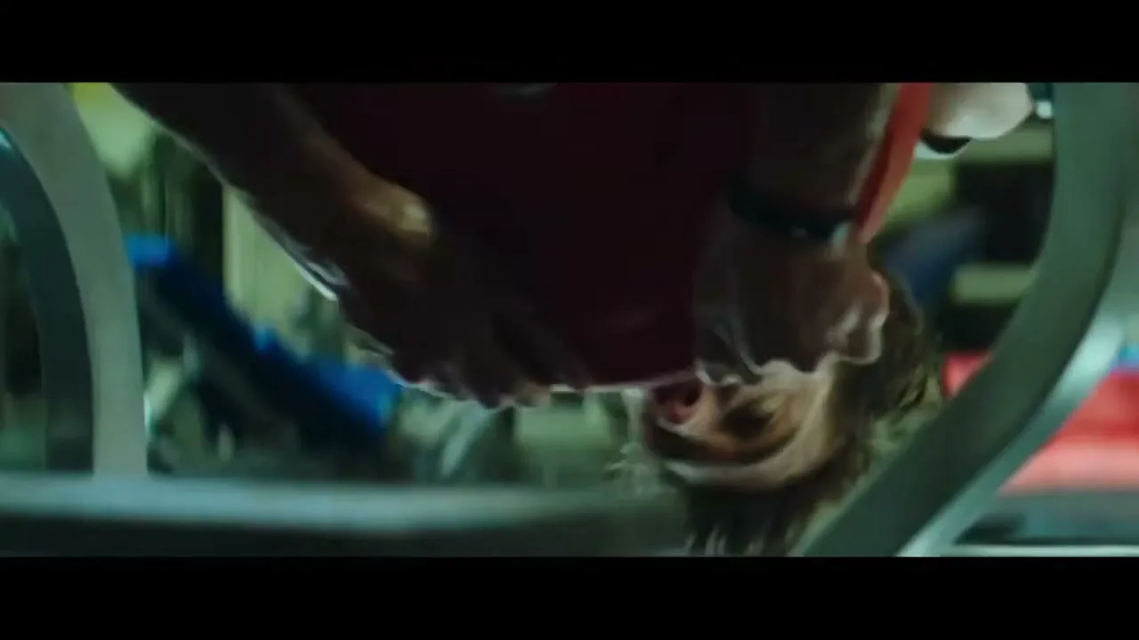 A male athlete, Michael Phelps, hangs upside down on an inversion table, his face strained during a workout in a gym.