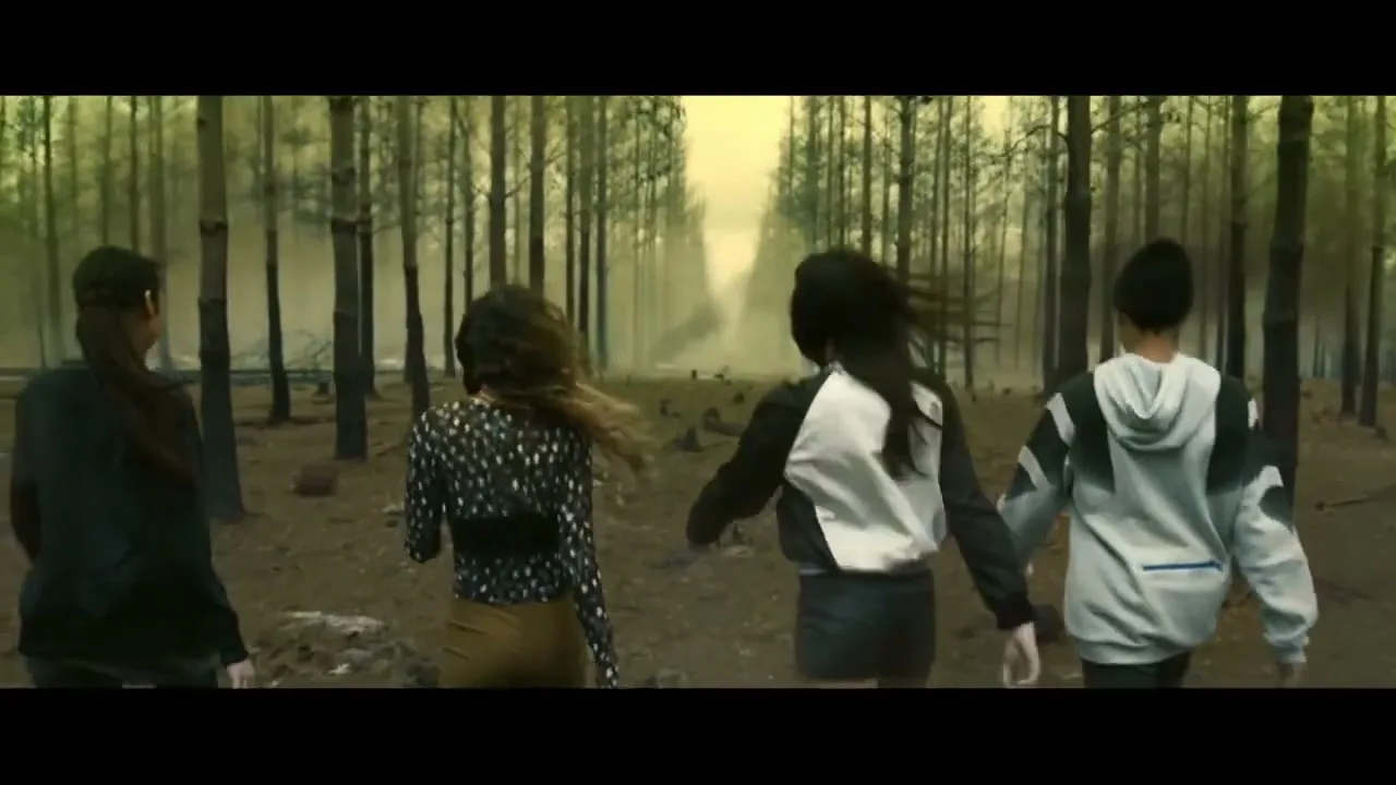 Four young people, dressed in casual streetwear, walk away from the camera through a desolate, misty forest, with one turning to look back.
