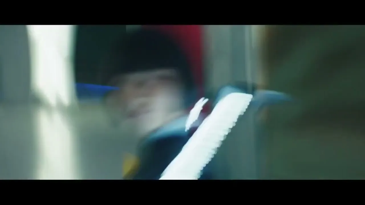 A young person with a bob haircut and dark clothing is seen in a blurry, fast-moving shot, with abstract white shapes in the foreground.