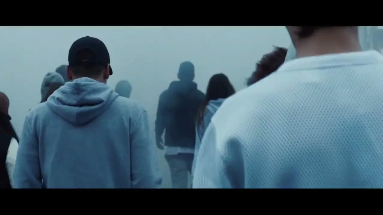 A diverse group of young people, dressed in casual streetwear, walk away from the camera into a thick, mysterious fog.