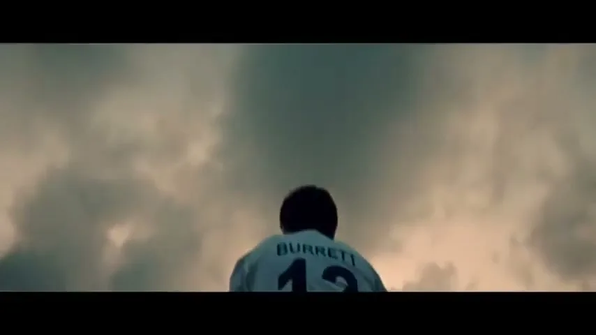 A female athlete in a white jersey with "BURRETT 12" on the back stands against a dramatic cloudy sky.