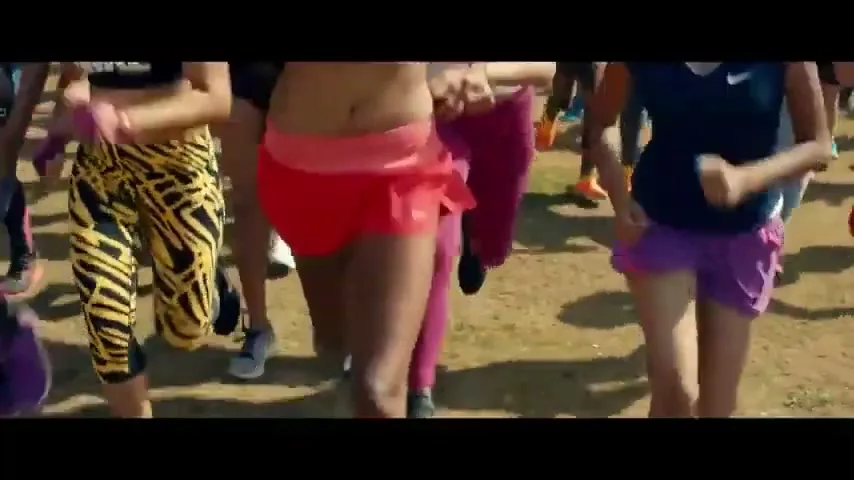 A diverse group of women in athletic wear run together on a dirt path, their shadows stretching long behind them in the bright sunlight.