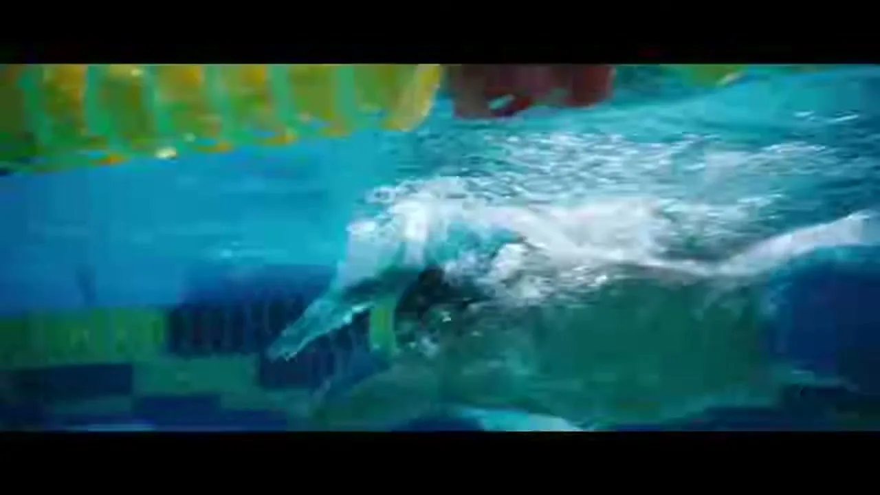 An underwater shot shows a male swimmer in a black cap and goggles, swimming freestyle in a pool with lane lines.