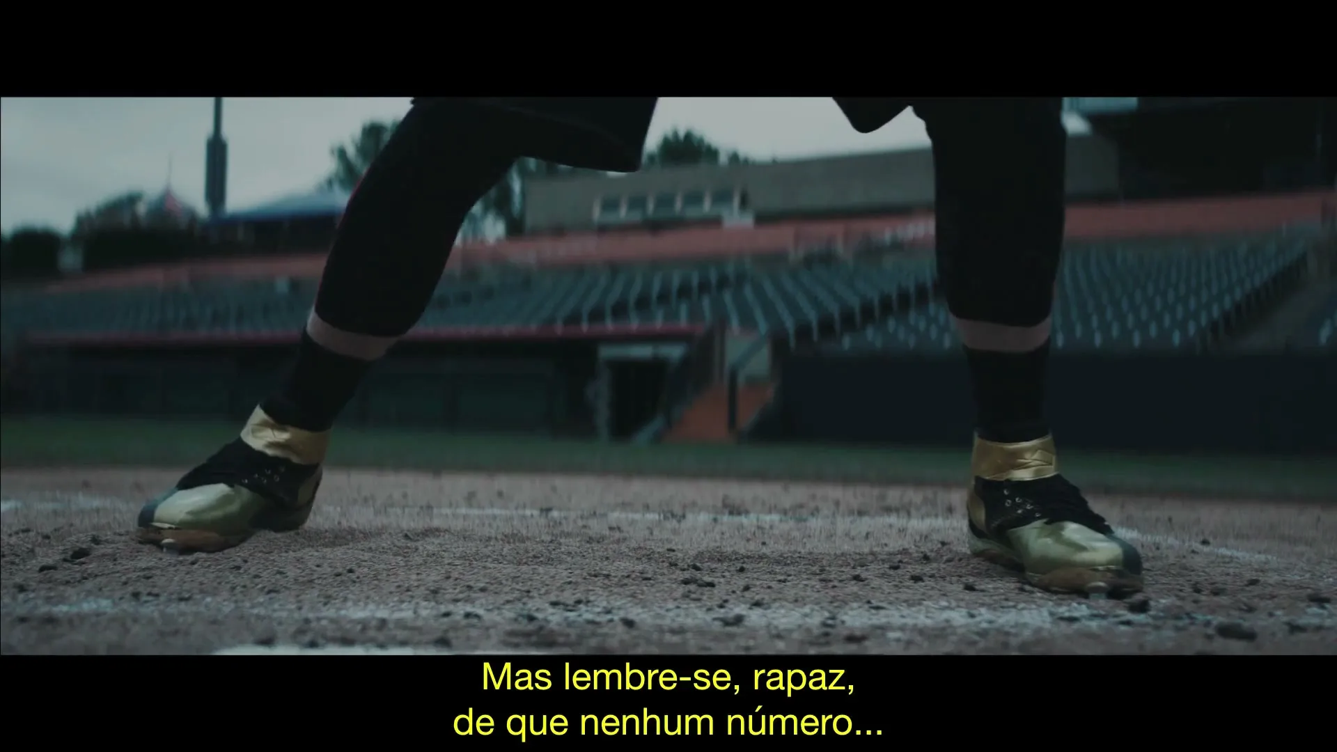 A baseball player in black and gold cleats and pants stands on a dirt mound in a stadium, preparing to pitch.