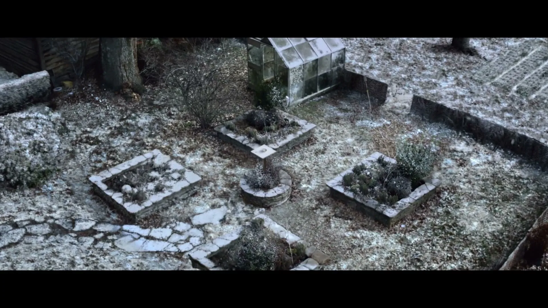 An overhead shot shows a snow-dusted garden with raised beds and a small greenhouse, evoking a serene winter landscape.