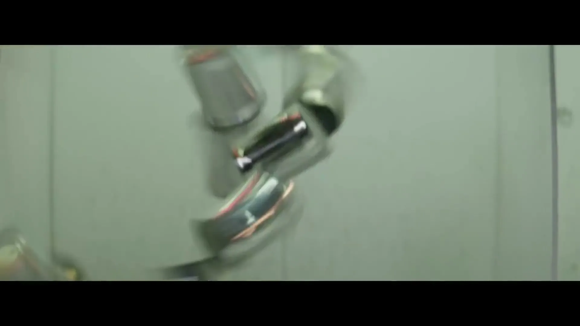 A stack of metal cans tumbles and falls against a light green wall, creating a sense of chaos and destruction.