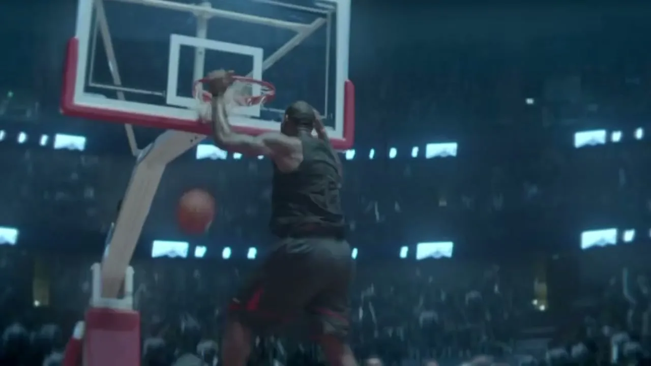 A male basketball player in a dark jersey dunks a basketball in a brightly lit stadium, with confetti falling.