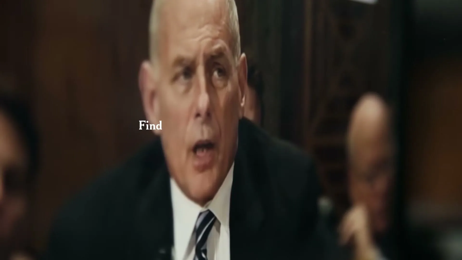 A bald, older man in a suit speaks at a formal meeting, with "to Find Out" text on screen.