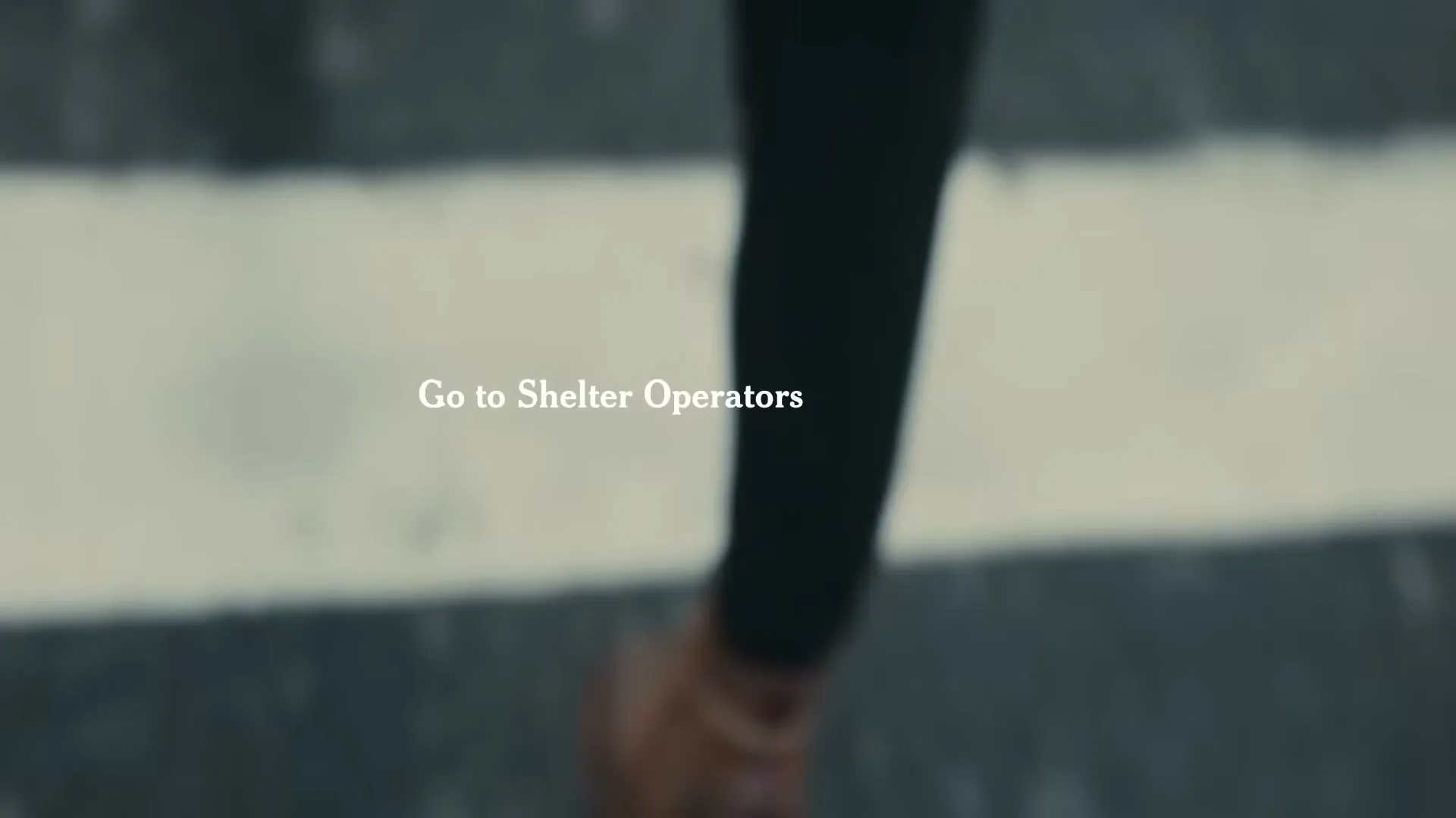 A person's legs and feet are seen walking on a wet, dark surface with white lines, as text appears and changes on screen.