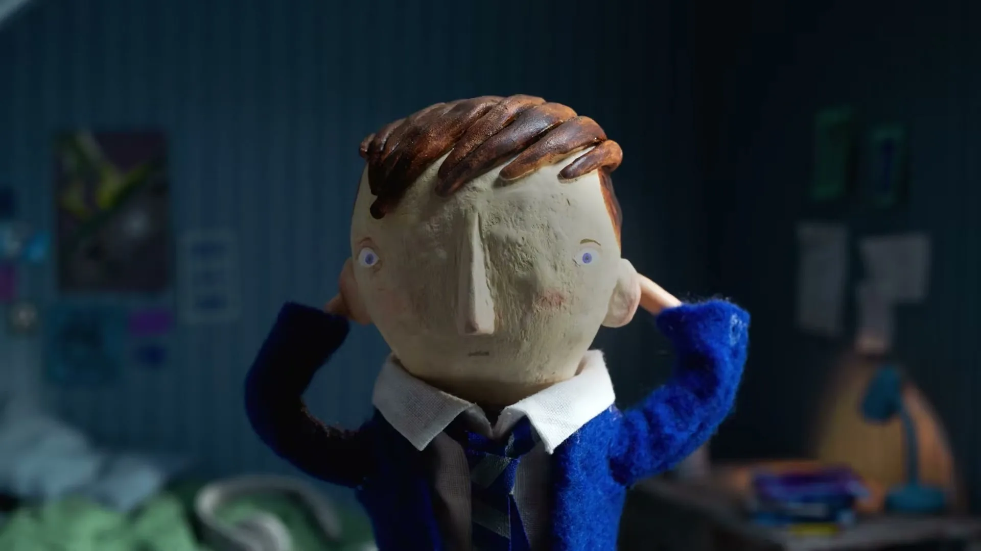 A stop-motion animated boy with blue hair pulls it off to reveal clay hair, looking distressed in his bedroom.