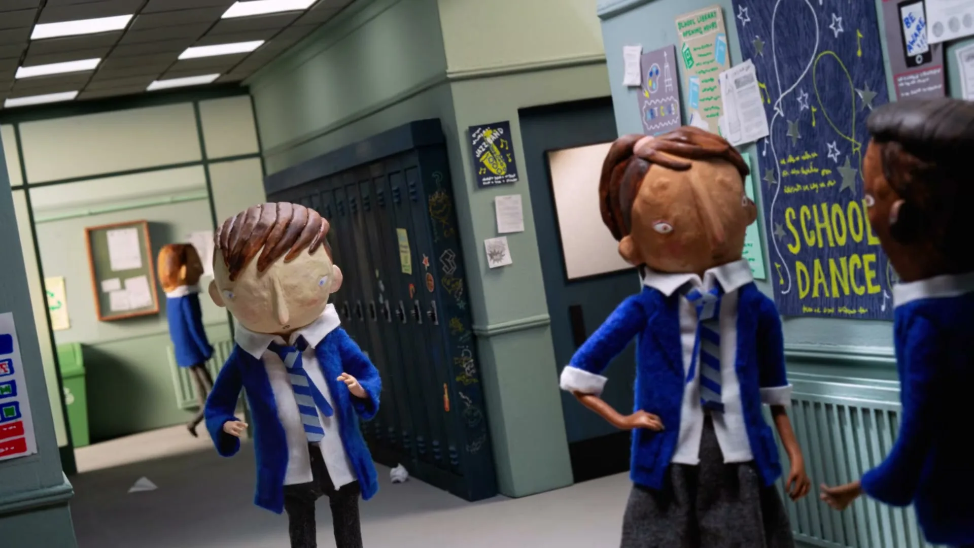 A stop-motion animated boy in a blue school uniform walks awkwardly in a school hallway, while two other students watch him.
