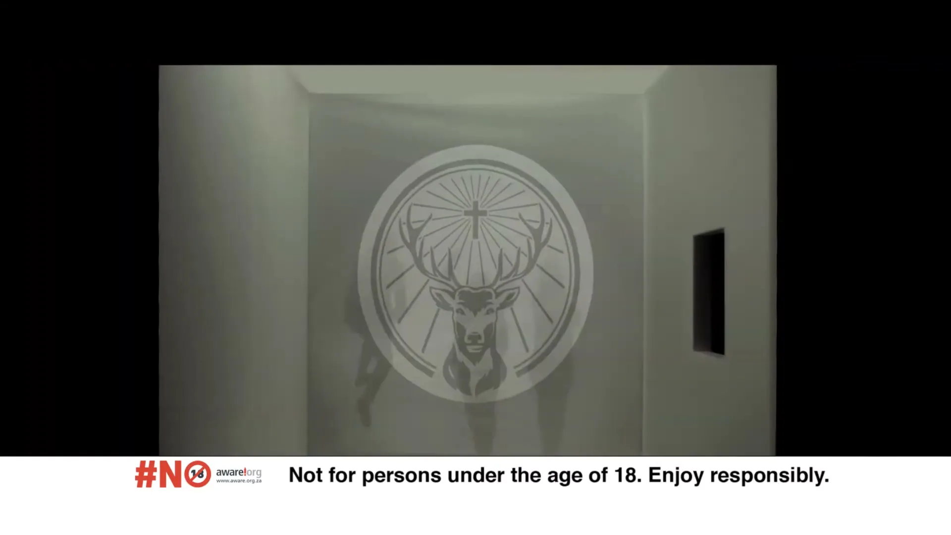 A Jägermeister logo is projected onto a white wall, then the wall breaks apart to reveal three people walking towards the camera.