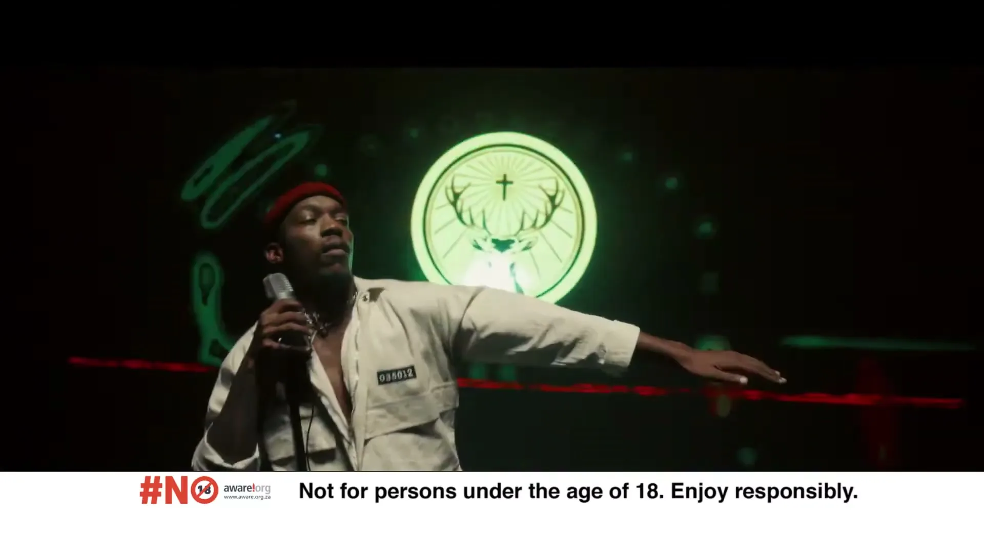 A male singer in a red beanie and white jumpsuit performs on stage, holding a microphone, with a large Jägermeister logo projected behind him.