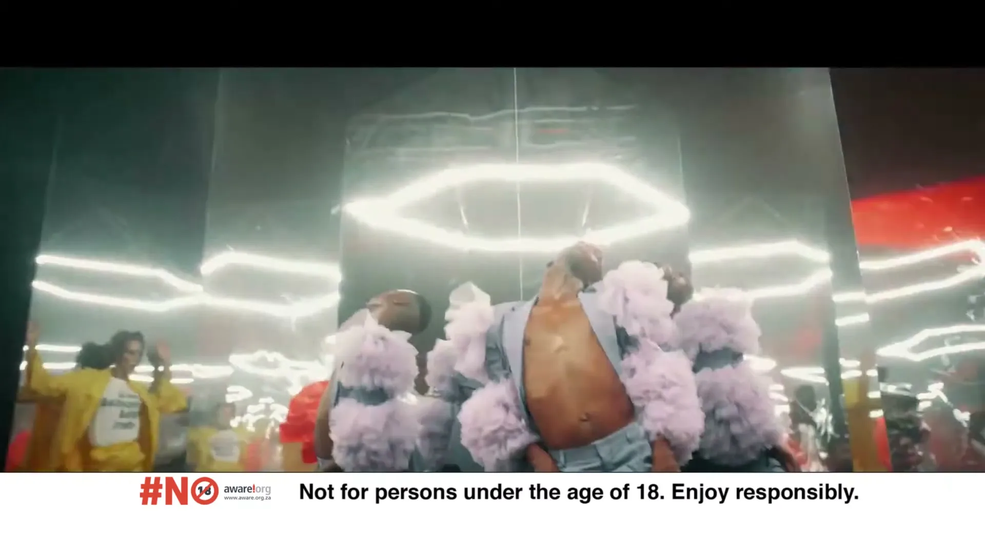A person in a light blue suit and fluffy shoulder pads dances in a dark room with neon lights, surrounded by reflections.