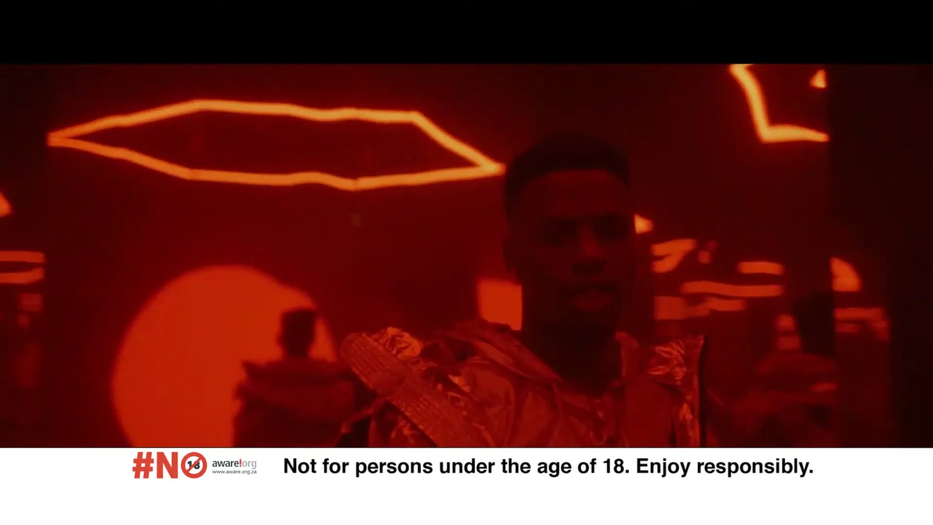 A man in his 20s, wearing a gold futuristic outfit, stands in a dark, red-lit virtual space with glowing orange lines.