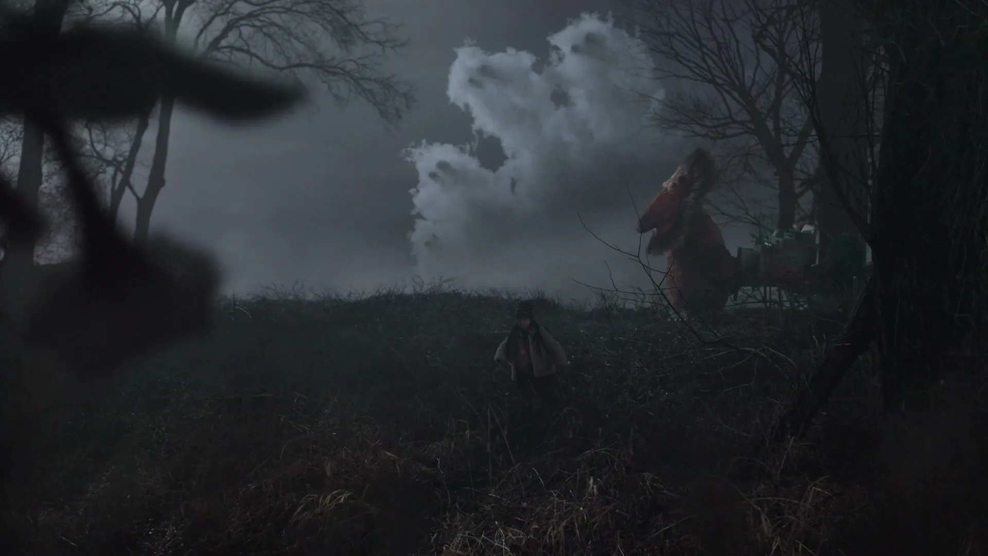 A small child in a white hat and coat walks through a dark, misty field towards a large, red, monster-like creature under a cloudy sky.