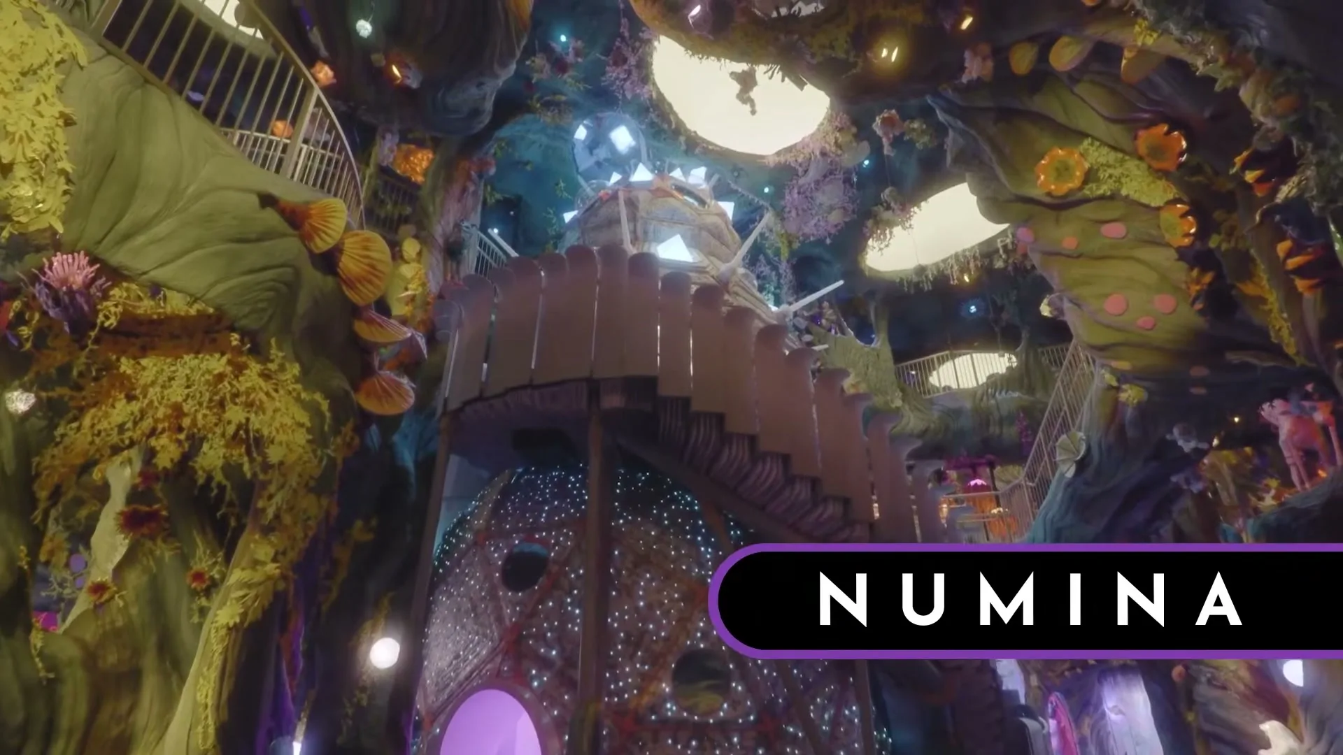 A wide shot of a fantastical, multi-level interior with glowing lights and organic shapes, featuring a central spiral staircase.