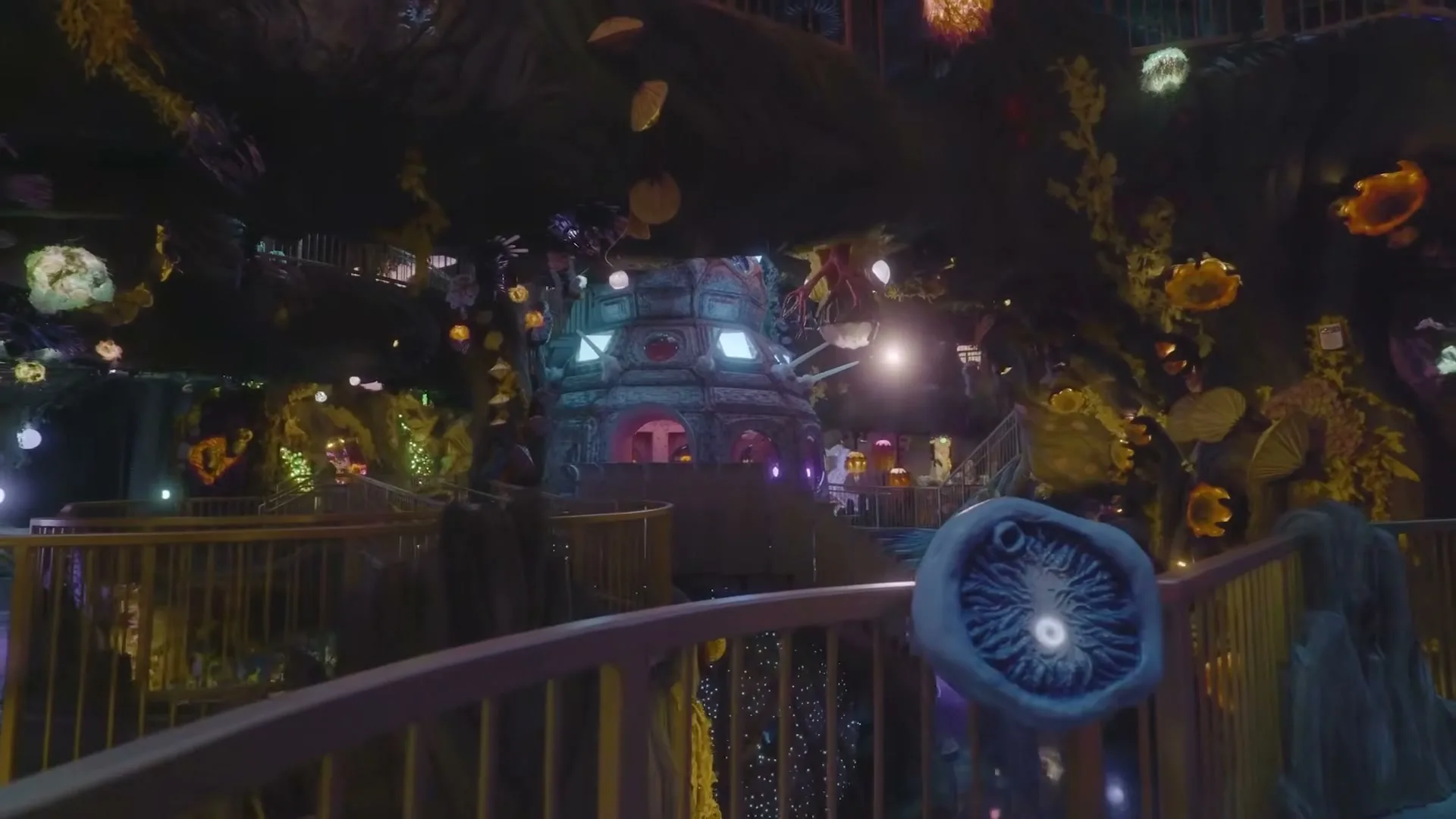 A wide shot of a fantastical, multi-level interior with glowing plants and structures, as a camera moves forward through the space.