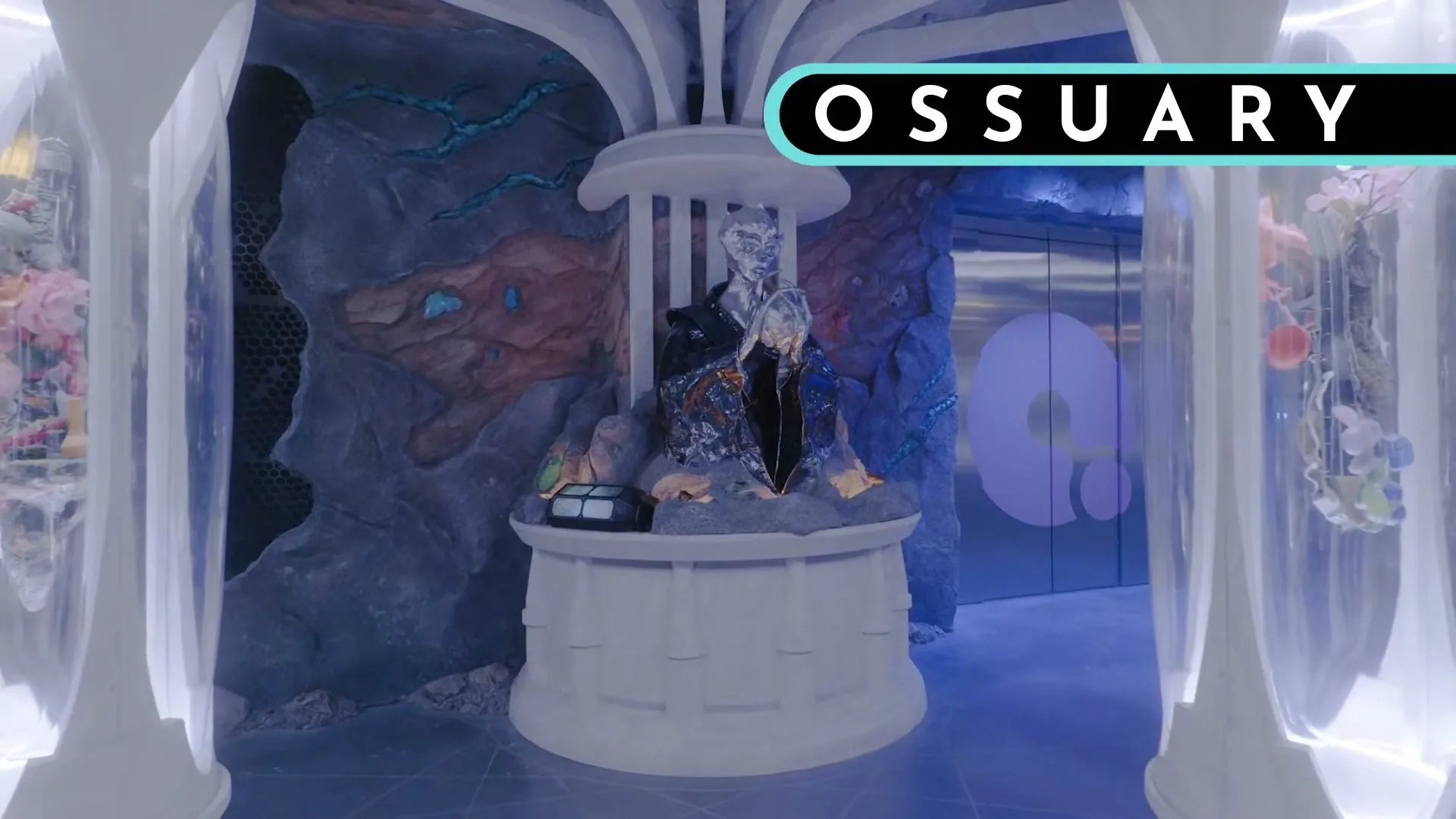 A wide shot of a fantastical, otherworldly room with a central figure on a pedestal, surrounded by glowing pillars and strange rock formations.