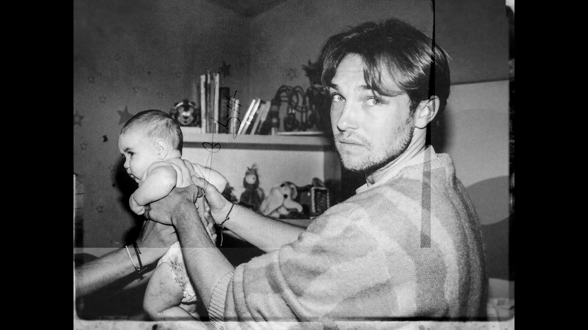A young man with a beard holds a baby in a diaper, looking at the camera in a black and white archival photo.