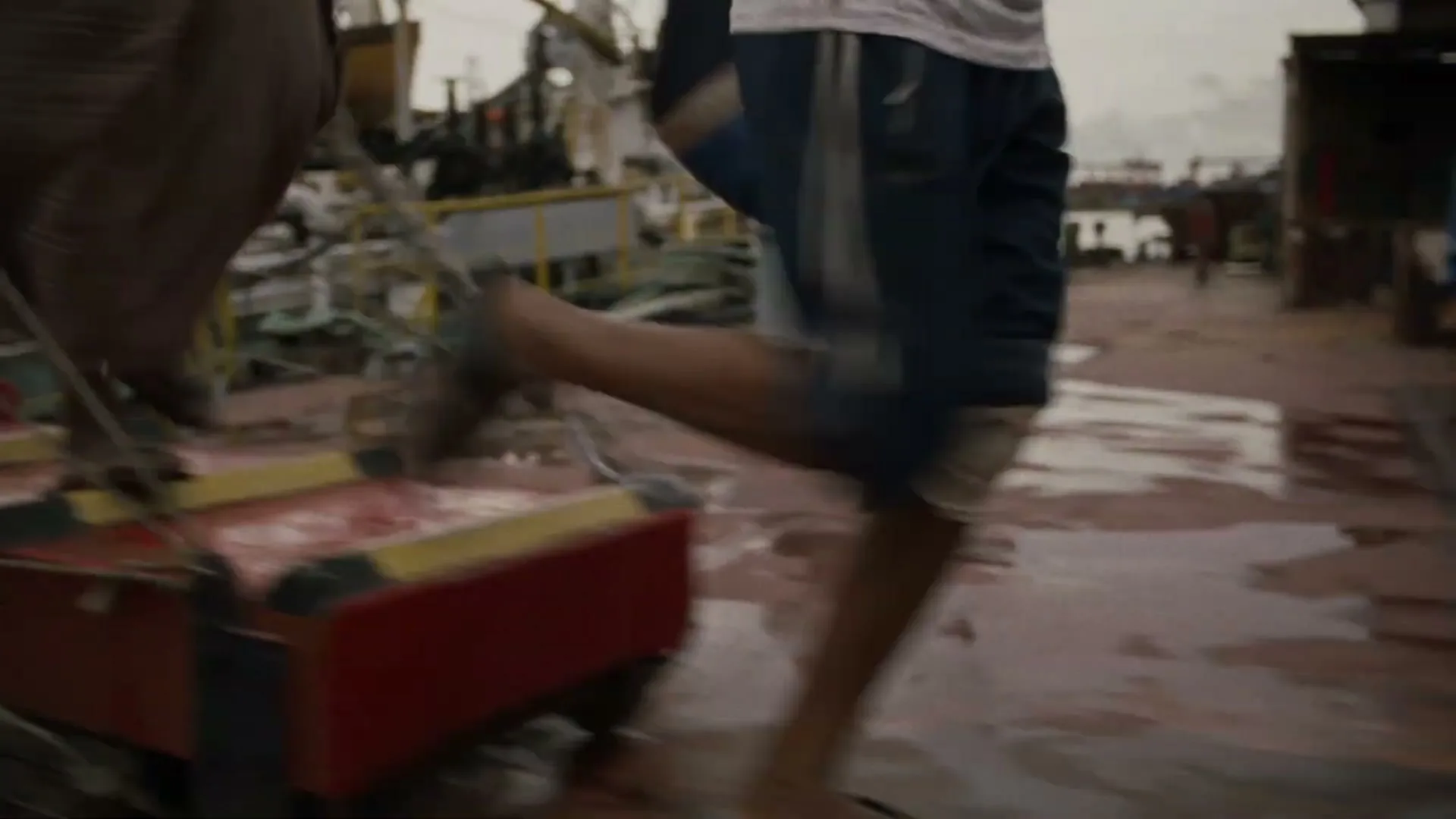 Two people, one with a bandaged leg, run across a wet, red gangplank on a boat deck, with debris and other boats in the background.