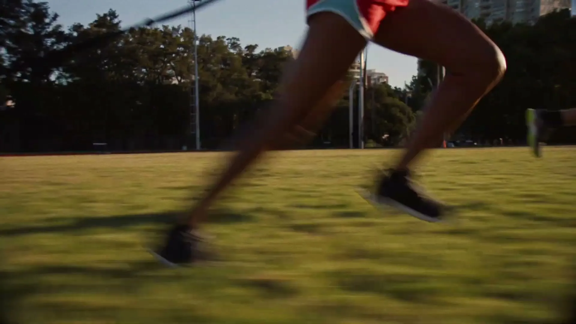 Two people run across a grassy field with trees and buildings in the background, as if training for a race.