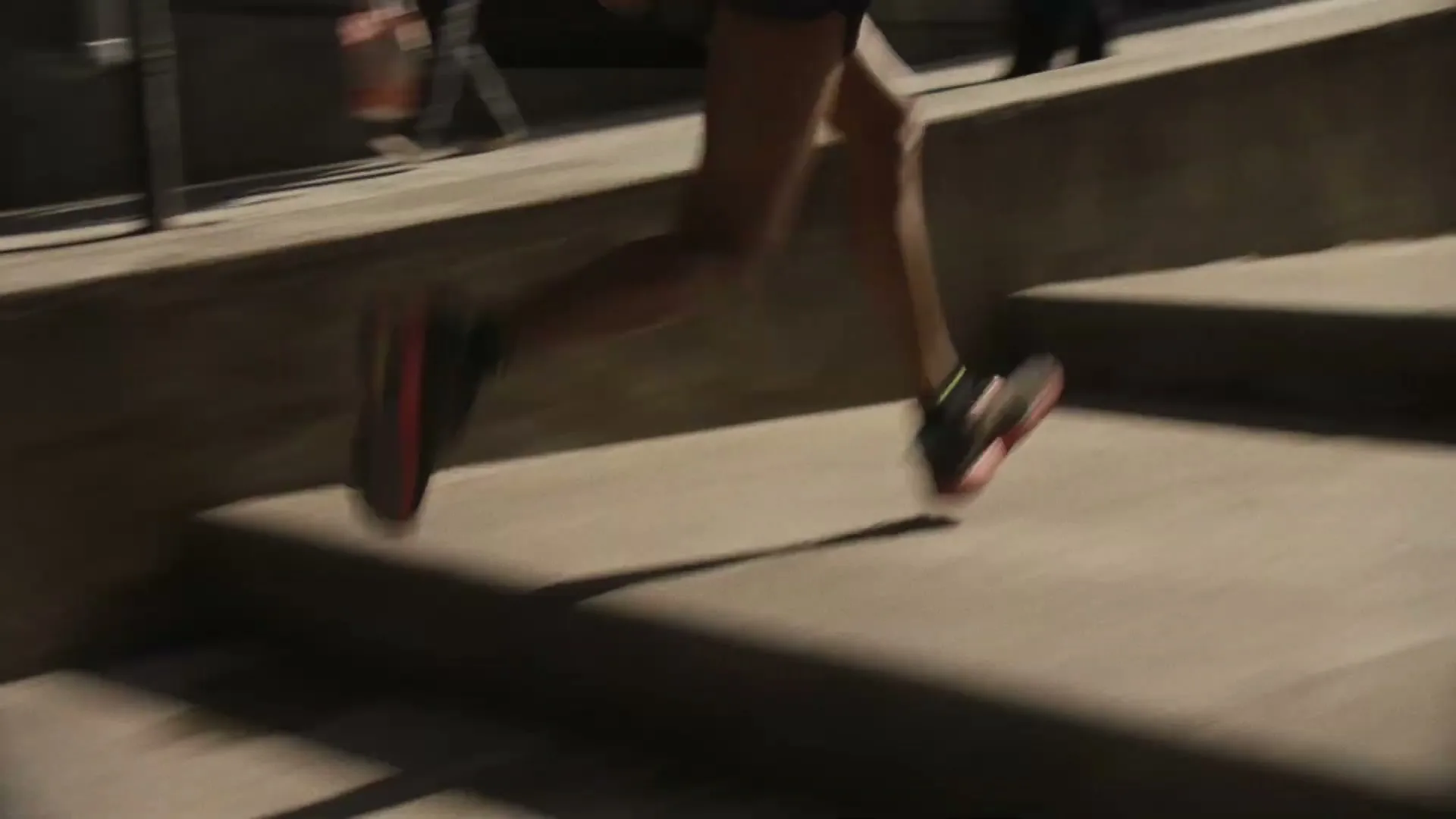 A person's legs and feet are seen running up concrete stairs, with motion blur, in a low-light setting.