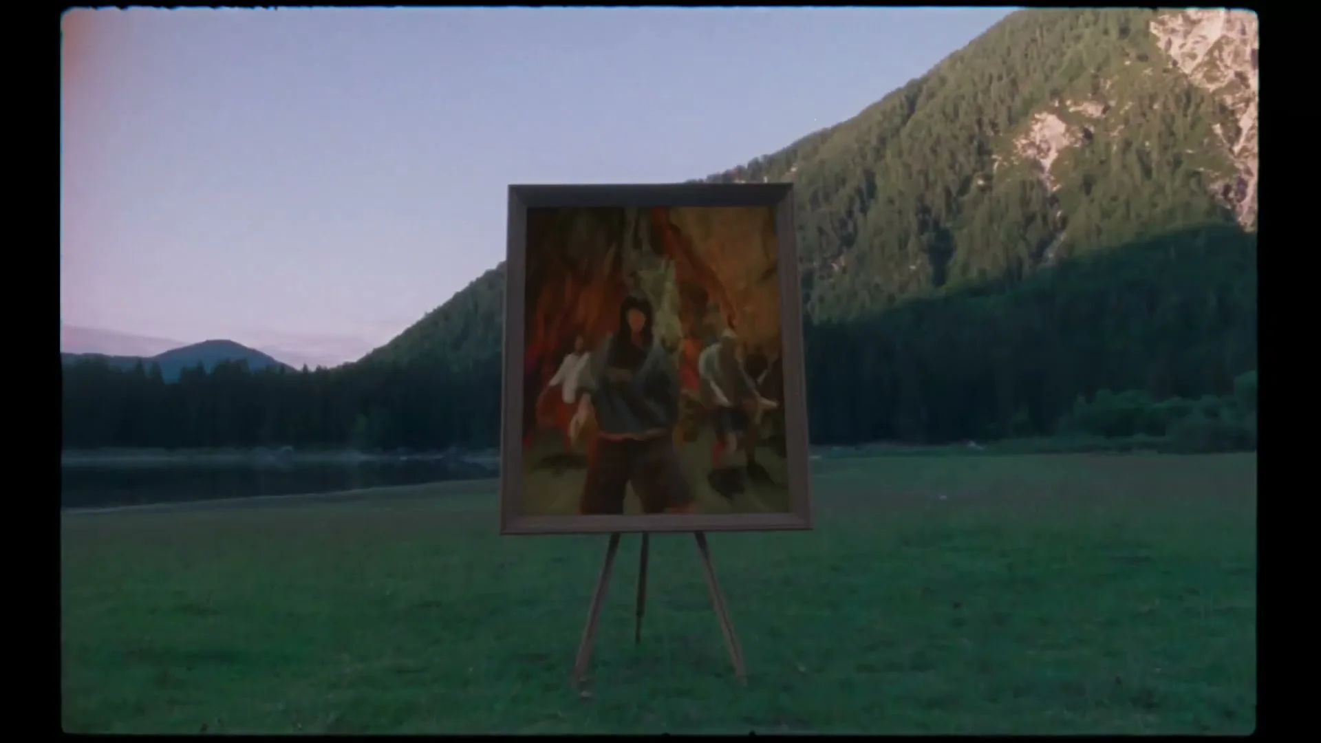 A painting on an easel in a grassy field depicts three people in a cave, with mountains and a lake in the background at dusk.