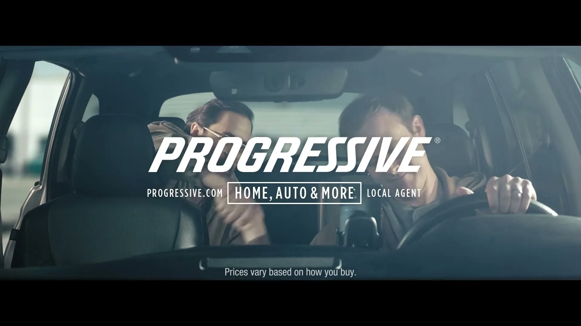 Two men, one driving and one in the passenger seat, are seen from the back seat of a car with the Progressive logo overlaid.