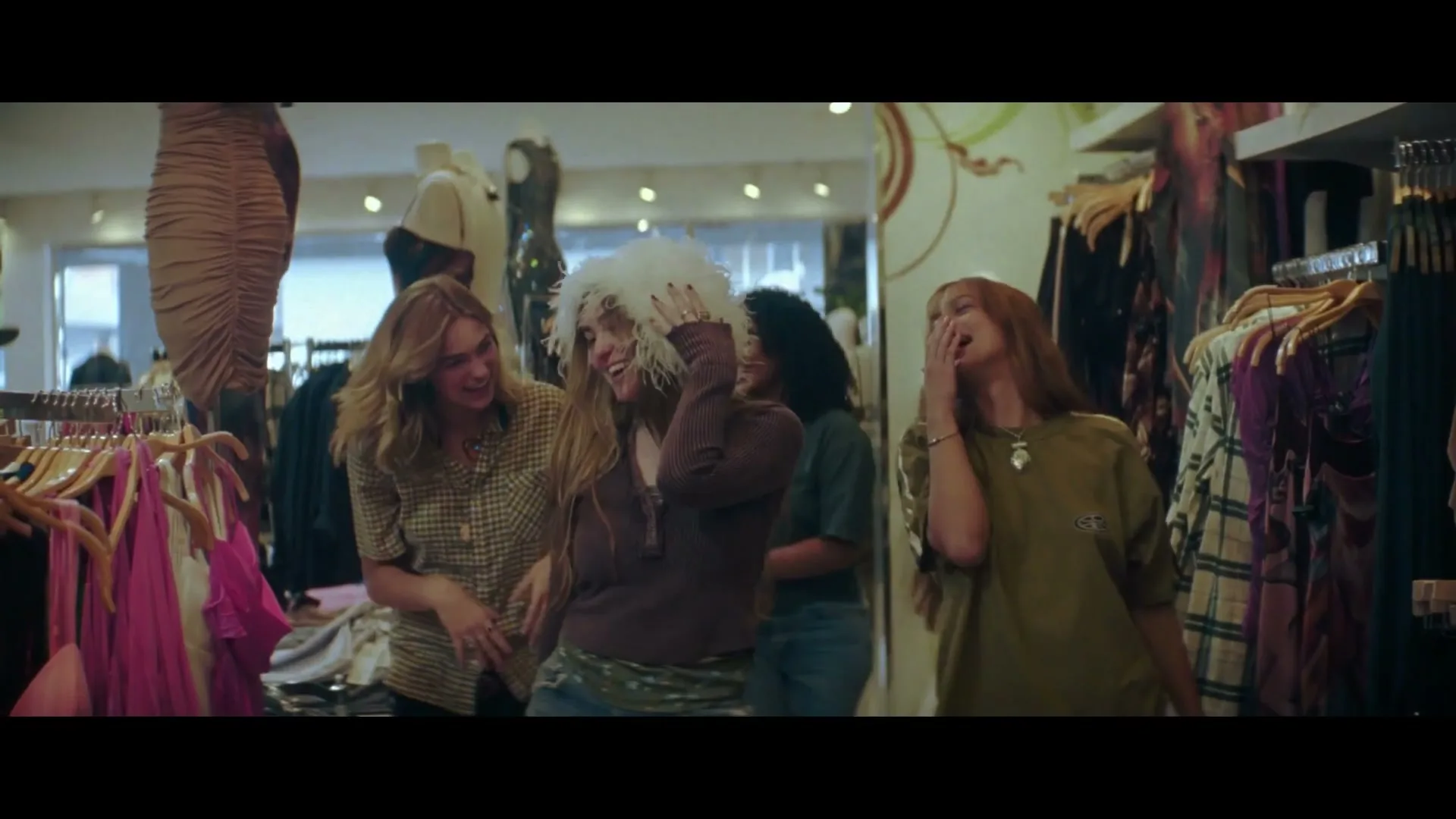 Three young women laugh and try on clothes in a brightly lit clothing store.