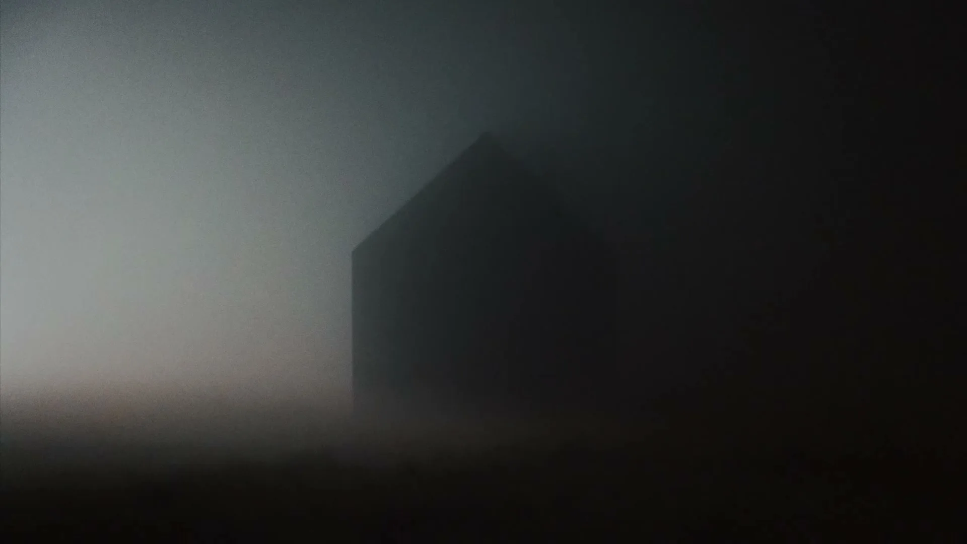 A dark, ominous house is barely visible through thick, grey fog, creating a mysterious and unsettling atmosphere.