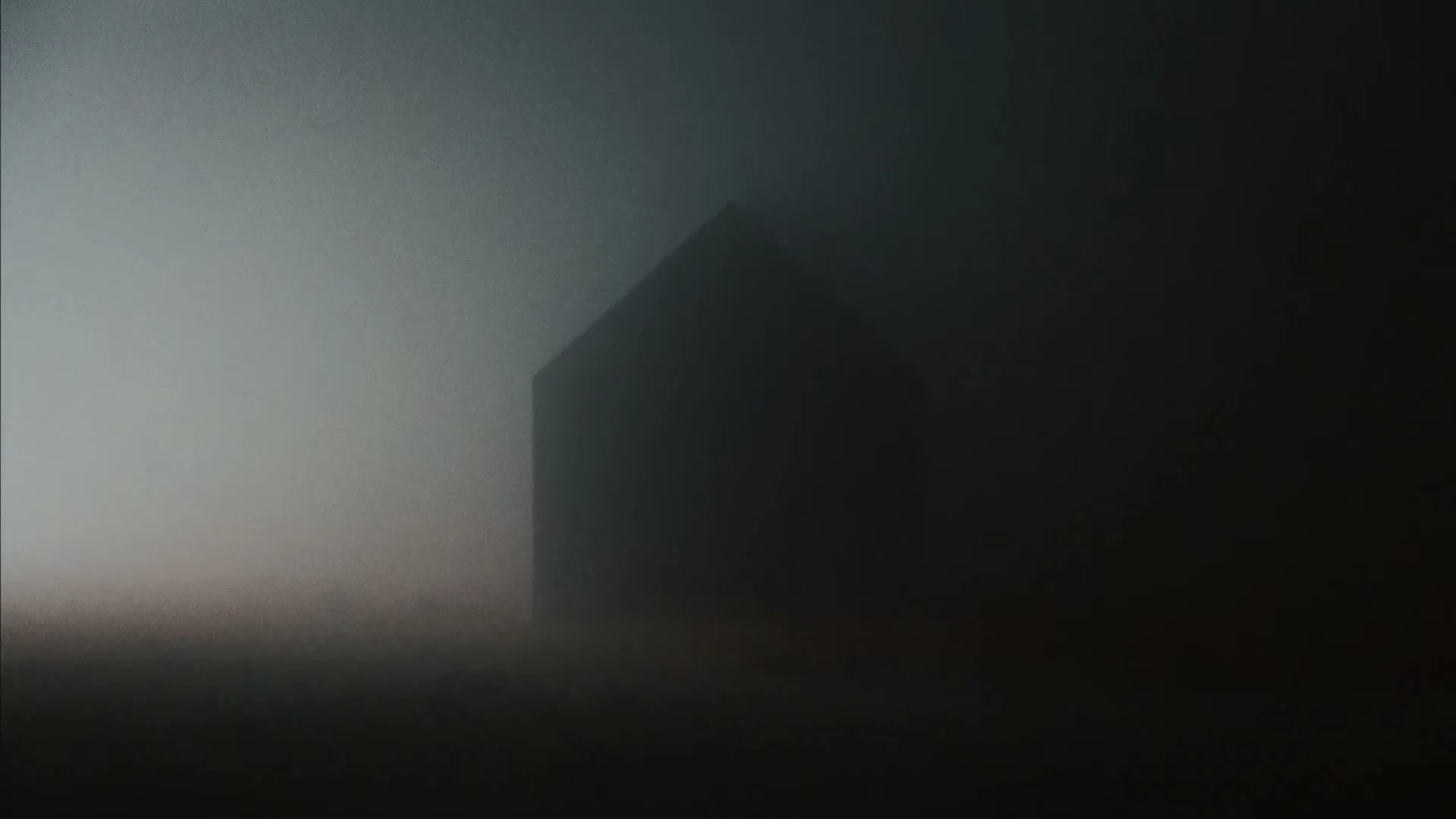 A dark, silhouetted house stands ominously in a thick, grey fog, creating a mysterious and unsettling atmosphere.