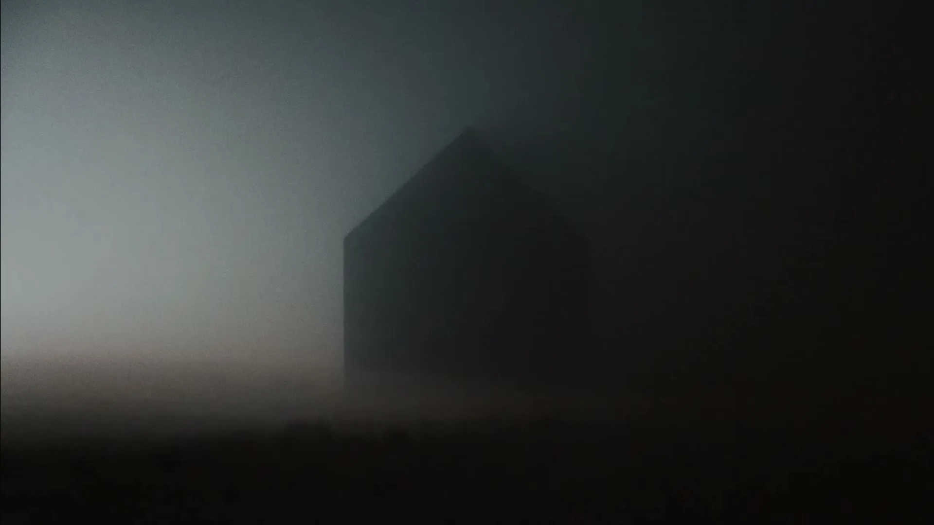 A dark, ominous, house-like structure is barely visible through thick, grey fog, creating a mysterious and unsettling atmosphere.