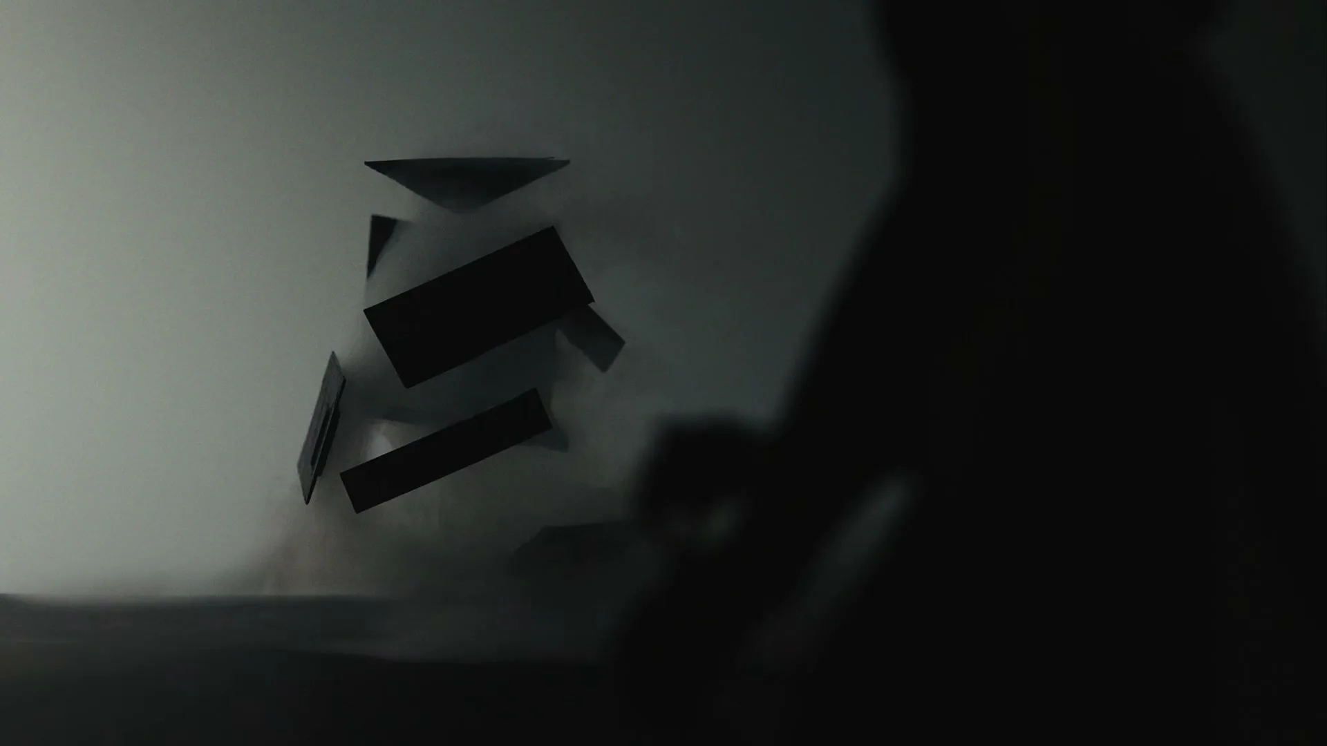 A silhouetted paper house model disintegrates into smoke and dust, with a blurred human figure in the foreground, against a dark, smoky background.