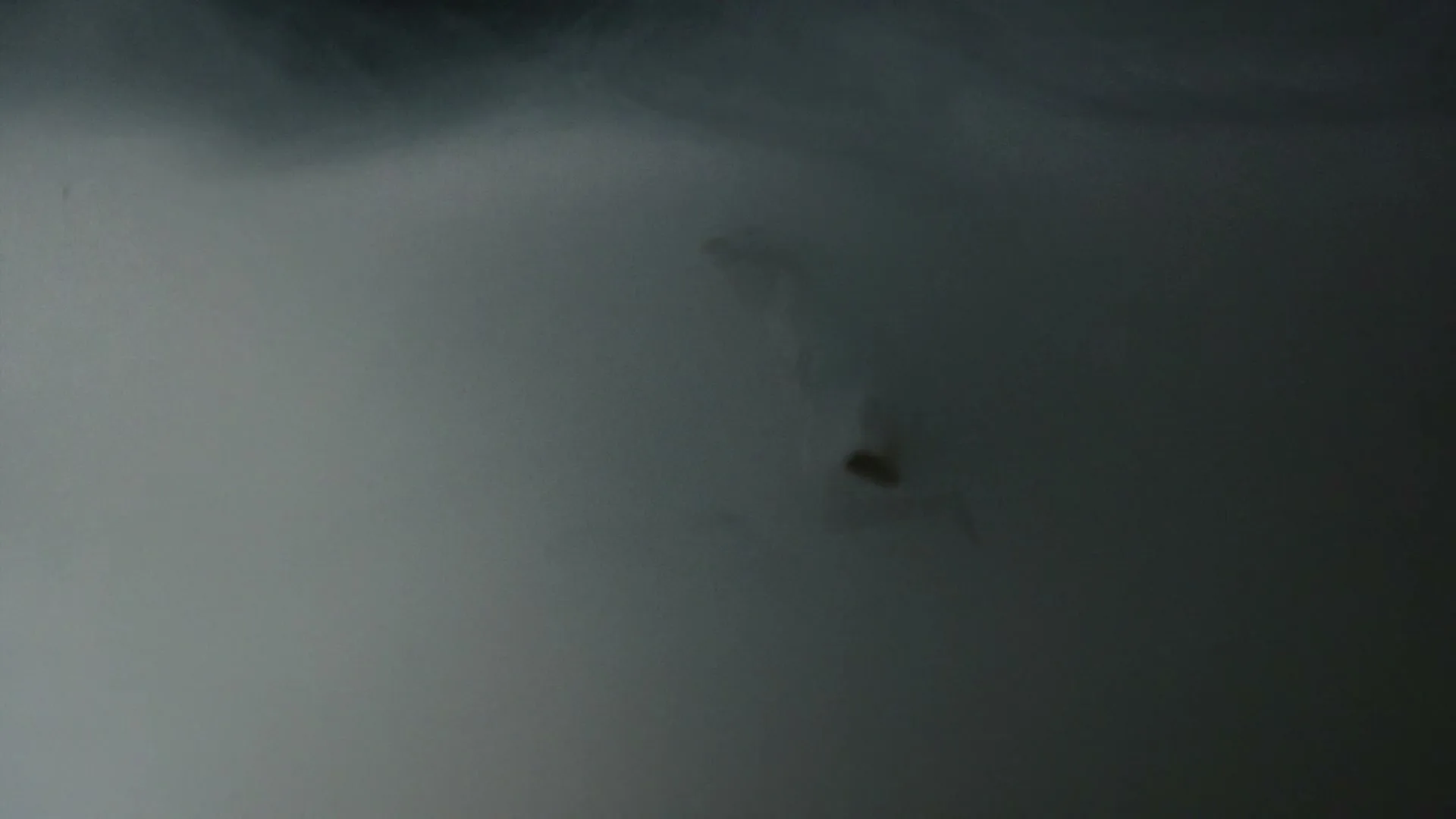 A person in light clothing is seen through a thick, smoky haze, appearing to float or fall in a dark, ambiguous space.