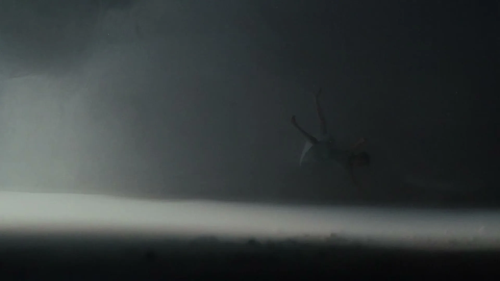 A person in light clothing falls through a dark, smoky void, with a bright light source at the bottom of the frame.