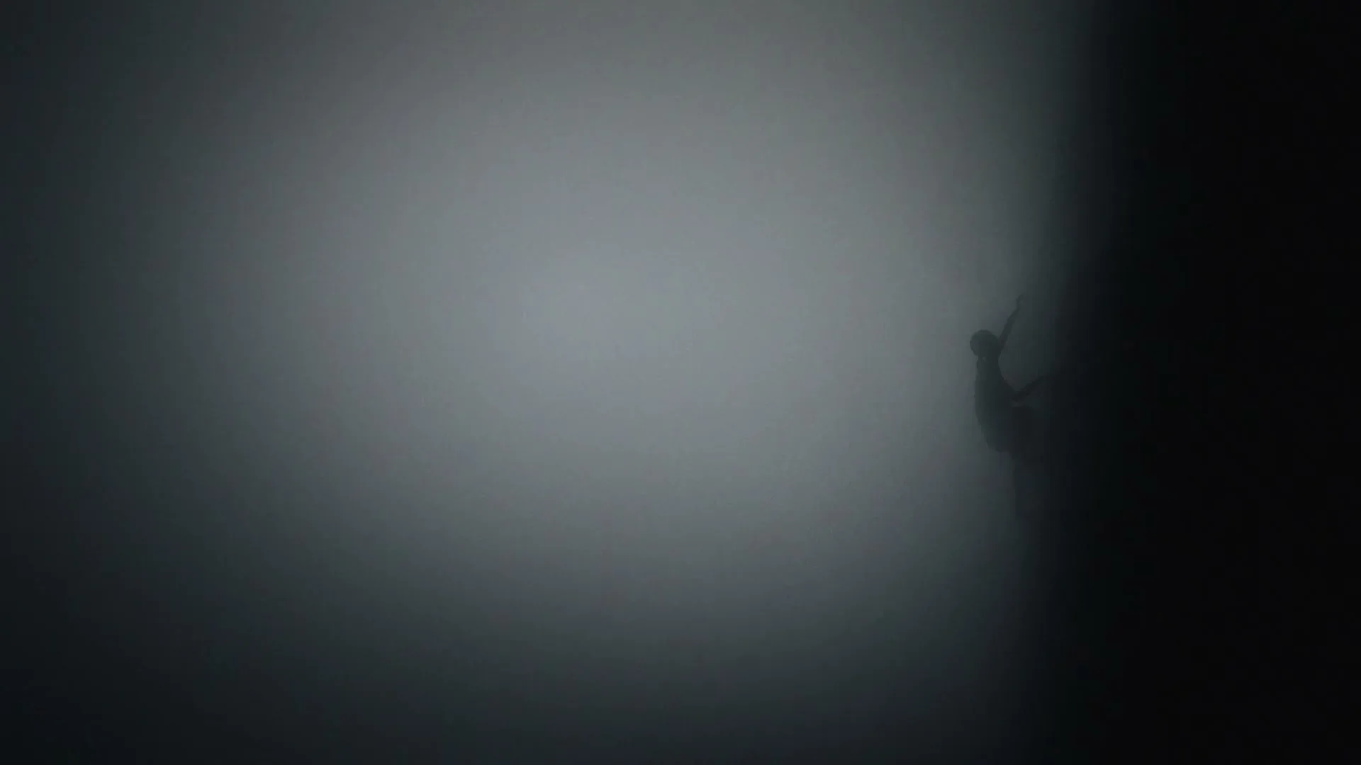 A lone, silhouetted figure is seen from a high angle, struggling to climb a dark, smoky wall in a mysterious, foggy environment.