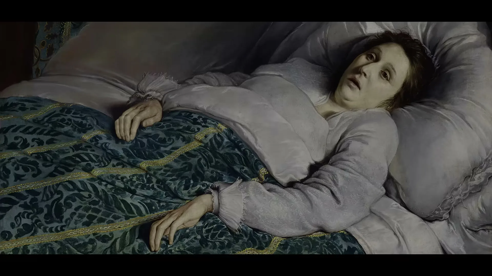 A woman with pale skin and dark hair lies in a bed with white sheets and a green patterned blanket, looking distressed.