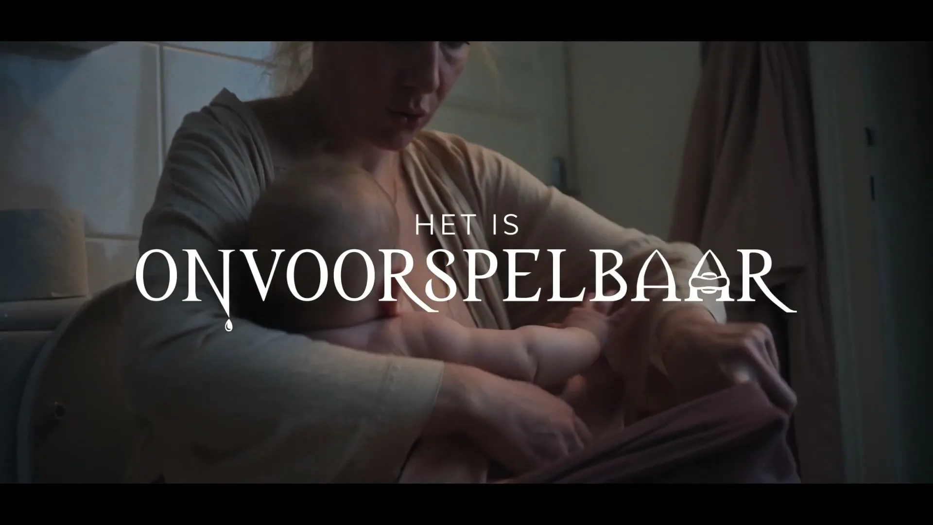 A woman with blonde hair, wearing a light-colored top, breastfeeds a baby while sitting on a toilet in a bathroom.